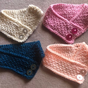 May include: Four crocheted neck warmers with button closures. The neck warmers are in pink, white, blue, and peach.