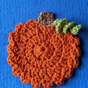 May include: A crocheted pumpkin with a brown stem and green leaves. The pumpkin is orange and has a textured surface.