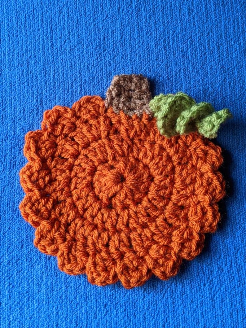 May include: A crocheted pumpkin with a brown stem and green leaves. The pumpkin is orange and has a textured surface.