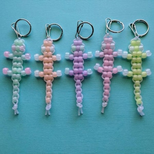 May include: Five beaded lizard keychains in different pastel colors: light green, peach, lavender, pink, and yellow. Each keychain has a silver ring.