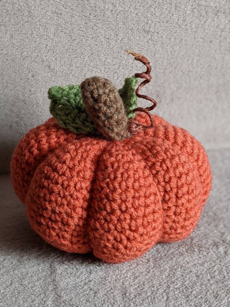 May include: A crocheted orange pumpkin with a brown stem and green leaves.