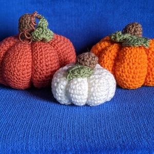 May include: Three crocheted pumpkins in different sizes and colors. The largest pumpkin is orange, the medium pumpkin is red, and the smallest pumpkin is white.