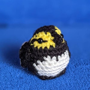 May include: A crocheted bird with black, white, and yellow yarn. The bird has black eyes and a white belly.
