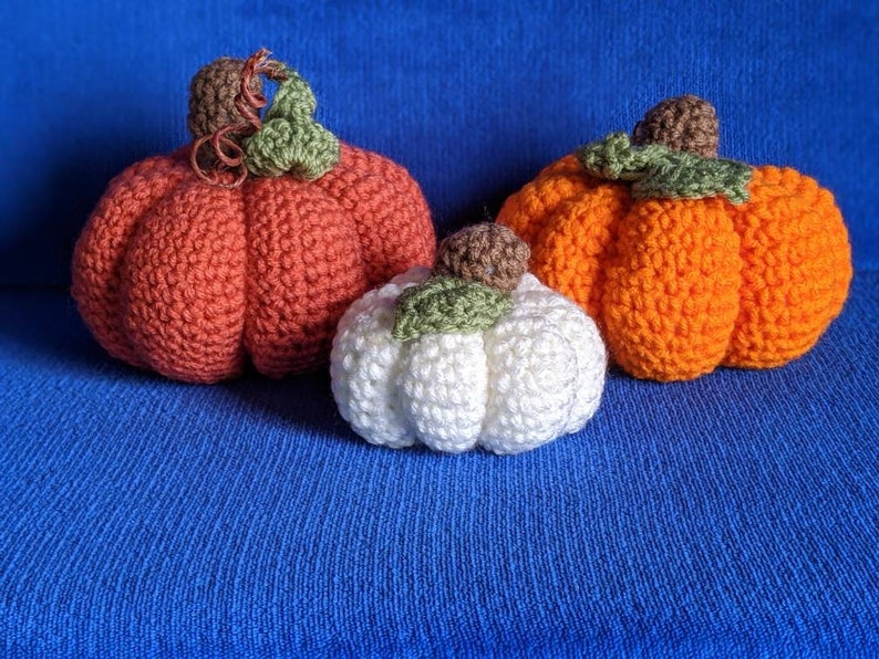 May include: Three crocheted pumpkins in different sizes and colors. The largest pumpkin is orange, the medium pumpkin is red, and the smallest pumpkin is white.