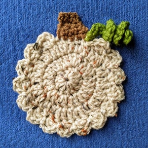 May include: A crocheted pumpkin with a brown stem and green leaves. The pumpkin is beige with brown and orange flecks.