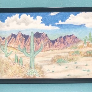 May include: A watercolor painting of a desert landscape with mountains in the background and cacti in the foreground. The sky is blue with white clouds. The mountains are a reddish-brown color and the cacti are green.