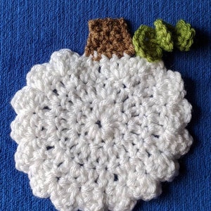 May include: White crocheted pumpkin with a brown stem and green crocheted leaves.