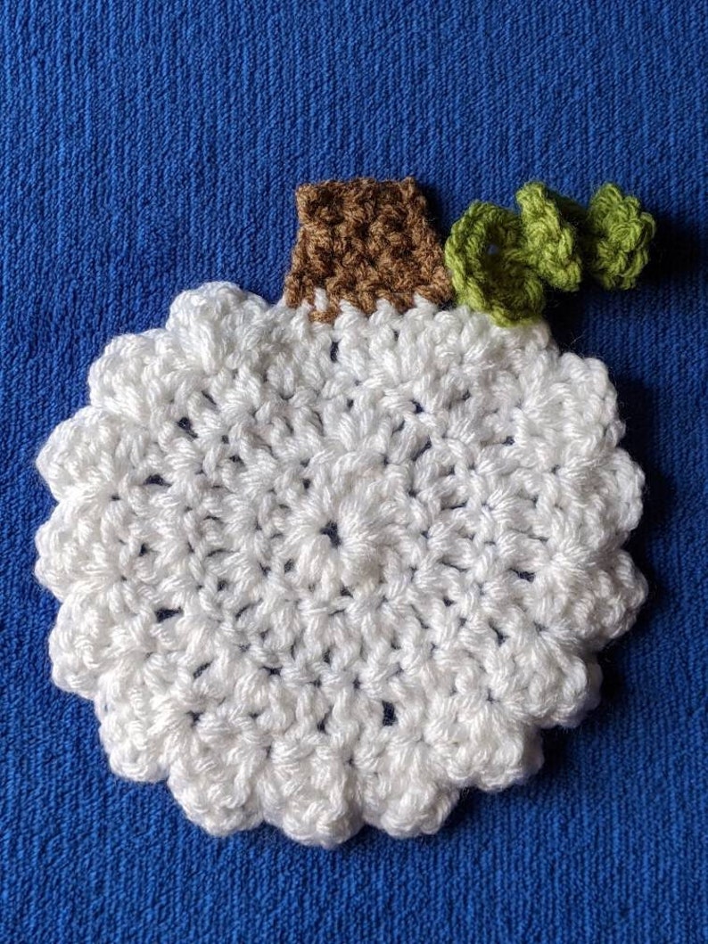 May include: White crocheted pumpkin with a brown stem and green crocheted leaves.