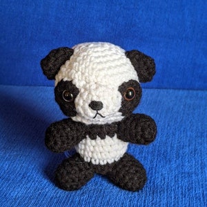 May include: A small crocheted panda bear toy with black and white fur. The panda has black eyes and a black nose.