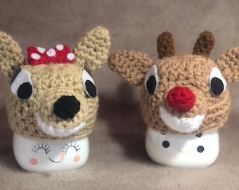 May include: Two crocheted reindeer mug toppers. One reindeer has a red bow with white polka dots. The other reindeer has a red nose.