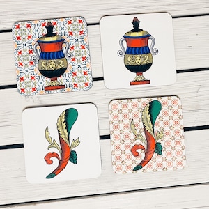 Op de afbeelding: Vier vierkante onderzetters met verschillende ontwerpen. De onderzetters zijn wit met een decoratief patroon. Een onderzetter heeft een rode, blauwe en gouden urn met een bloemmotief. Een andere onderzetter heeft een groen en rood gestileerd bloemmotief. De overige twee onderzetters hebben een herhalend patroon van kleine bloemen.