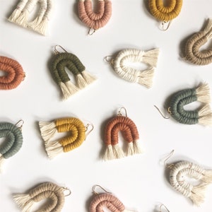 Peut inclure: Assortiment de boucles d'oreilles arc-en-ciel faites à la main dans différentes couleurs, notamment le vert, le marron, le beige, le blanc et le rose. Chaque boucle d'oreille présente un design arc-en-ciel à double couche avec des glands blancs.