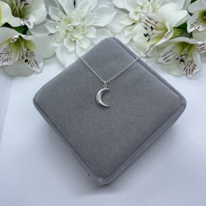 May include: A silver crescent moon pendant necklace on a silver chain, displayed in a gray velvet jewelry box.