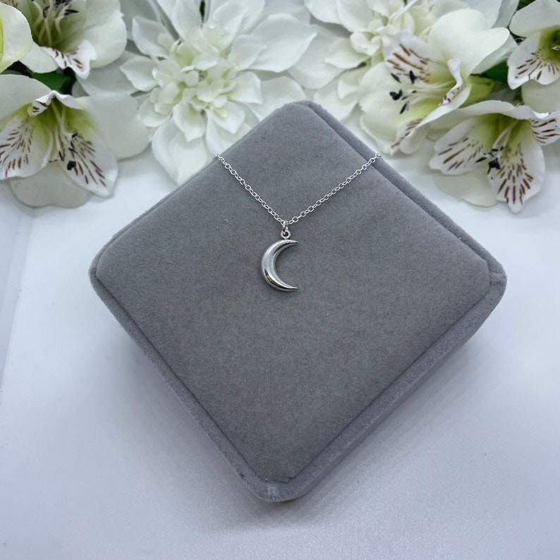 May include: A silver crescent moon pendant necklace on a silver chain, displayed in a gray velvet jewelry box.