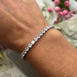May include: A silver bracelet with a row of clear round stones. The bracelet is on a person's wrist.