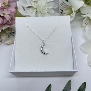 May include: A silver crescent moon pendant necklace on a silver chain, displayed in a white box.