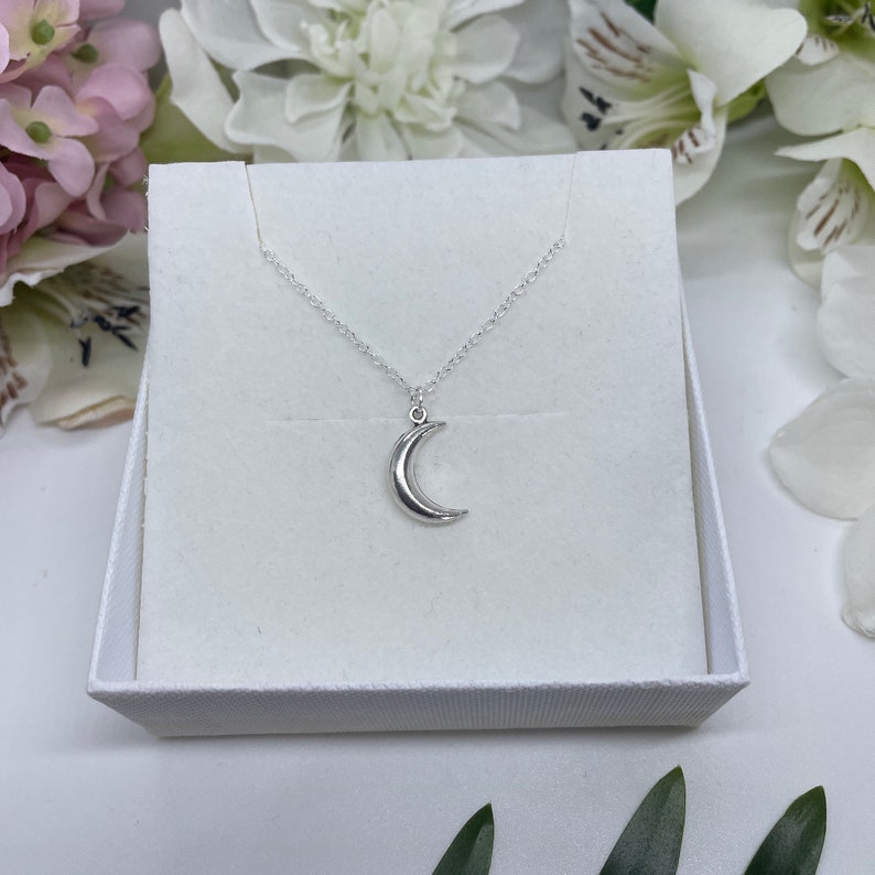 May include: A silver crescent moon pendant necklace on a silver chain, displayed in a white box.