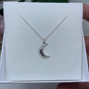 May include: A silver crescent moon pendant necklace on a silver chain. The necklace is displayed in a white box.