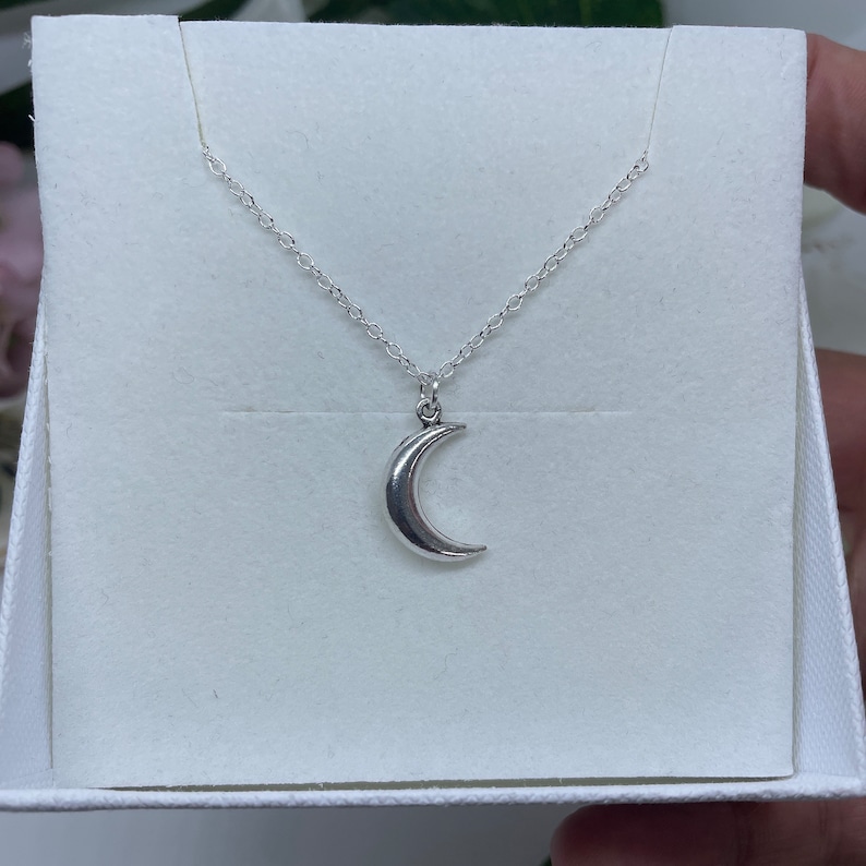 May include: A silver crescent moon pendant necklace on a silver chain. The necklace is displayed in a white box.