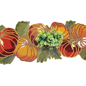 May include: A beaded table runner featuring pumpkin and leaf designs in shades of orange, red, and green. The pumpkins have a textured appearance and are arranged with green foliage in the center. A festive autumn decoration.