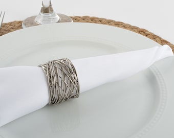 May include: A white napkin is wrapped around a silver metal napkin ring. The napkin ring is made of thin, interwoven metal wires.