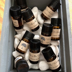 May include: A wooden box filled with small glass bottles containing essential oils. The bottles are labeled with the text "Walk in the Woods" and "Walk in the Woods Cypress, Siberian Fir, Cedarwood".