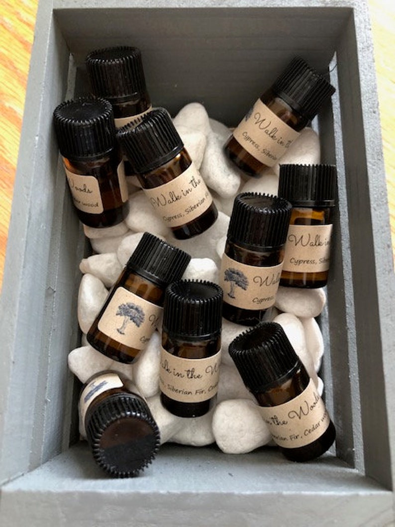 May include: A wooden box filled with small glass bottles containing essential oils. The bottles are labelled with the text "Walk in the Woods" and "Walk in the Woods Cypress, Siberian Fir, Cedarwood".