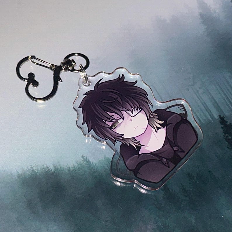 May include: A clear acrylic keychain featuring an anime-style character with black hair and a black hoodie. The keychain has a silver clasp and a heart-shaped accent. The character has a neutral expression.