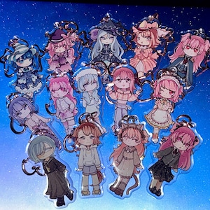 May include: A selection of clear acrylic keyrings showcasing anime-style characters with diverse hairstyles and attire. Each keyring has a silver metal ring. The characters are in shades of pink, blue, and purple.