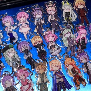 May include: A selection of anime-style character keyrings. Each keyring showcases a unique character design with vibrant colours, including pink, purple, green, and gold. The keyrings are attached to silver-coloured metal rings.