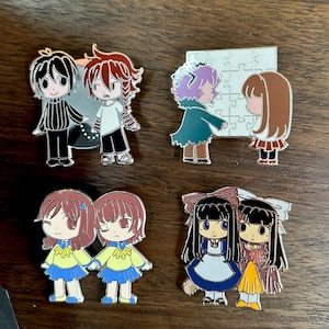 May include: Set of eight enamel pins featuring characters from the video game "The Crooked Man." The pins are colourful and feature a variety of characters, including a boy with red hair, a girl with brown hair, and a girl with purple hair.