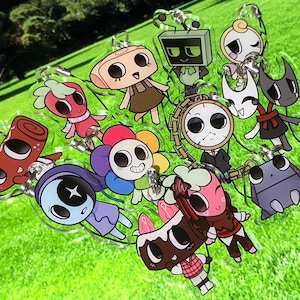 Könnte beinhalten: Eine Sammlung bunter Cartoon-Charakter-Schlüsselanhänger mit verschiedenen Designs, darunter eine Erdbeere, ein Roboter und eine Blume. Die Schlüsselanhänger sind aus klarem Acryl gefertigt und haben silberne Schlüsselringe. Der Hintergrund ist ein verschwommenes Grün.