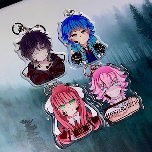 May include: Four anime-style character keychains. The keychains feature characters with various hair colors, including black, blue, and pink. Each character has a unique design and expression, with some featuring blood-like accents and text that says "OK" and "REDACTED".