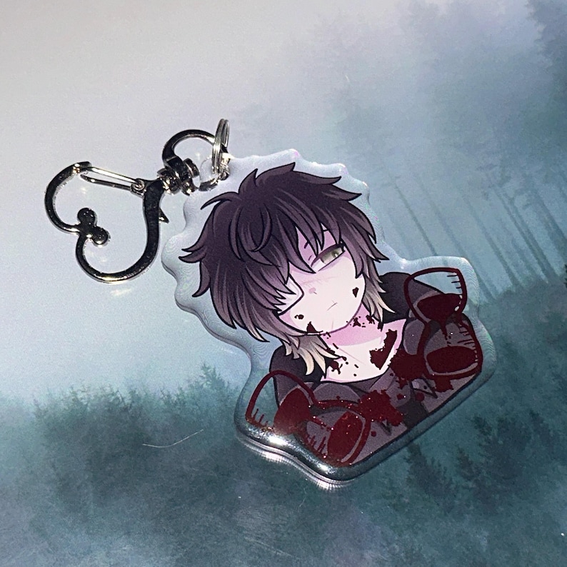 May include: A clear acrylic keychain featuring an anime-style illustration of a person with dark hair and blood-like splatters. The keychain has a silver-colored clasp.