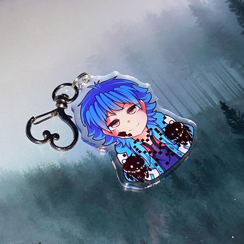 May include: A clear acrylic keychain featuring a cartoon character with blue hair and a blue jacket. The character has a smiling expression and is attached to a silver-colored clasp.