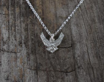 May include: A silver necklace with a small, detailed silver pendant shaped like the United States Air Force emblem.