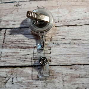 Pu&ograve; includere: Un portabadge retrattile trasparente con una clip in metallo color argento e un cinturino in plastica trasparente. Il portabadge ha una chiusura a scatto in metallo color argento. Il portabadge &egrave; progettato per contenere un badge identificativo o altri piccoli oggetti.