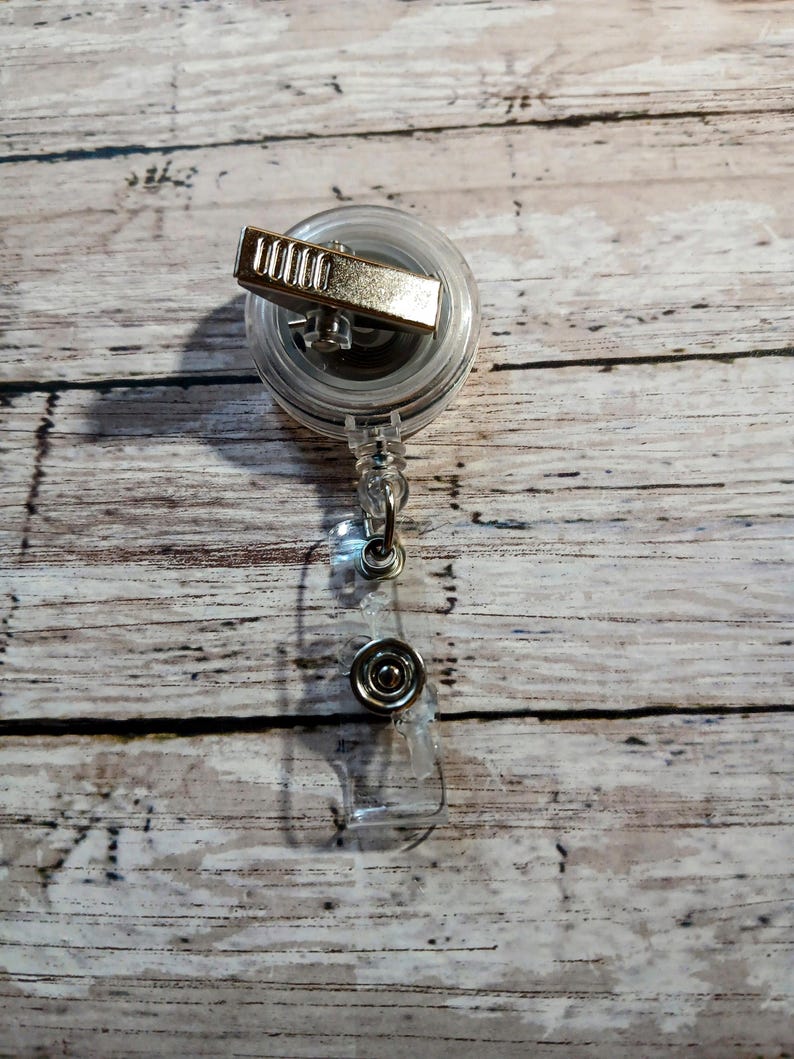 Pu&ograve; includere: Un portabadge retrattile trasparente con una clip in metallo color argento e un cinturino in plastica trasparente. Il portabadge ha una chiusura a scatto in metallo color argento. Il portabadge &egrave; progettato per contenere un badge identificativo o altri piccoli oggetti.