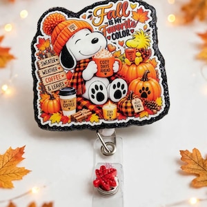 May include: A black glittery badge reel featuring a cartoon dog wearing an orange beanie and scarf, holding a mug labeled Cozy Days Ahead. The design includes pumpkins, autumn leaves, and text reading Fall Is My Favorite Color, Sweater Weather, Coffee & Leaves, and But First Coffee.