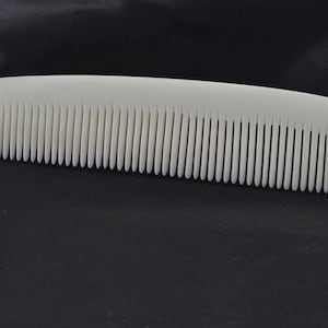 May include: A solid white hair comb with a smooth, curved top edge and a long row of fine, evenly spaced teeth. The comb features a simple, elongated design with rounded ends, presenting a clean and uniform appearance throughout the entire object.