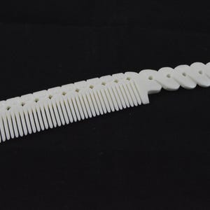 Puede incluir: Un peine de plástico blanco con un mango ondulado único. El peine tiene dientes finos y está diseñado para desenredar el cabello.