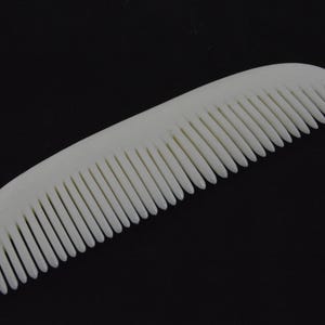 Könnte beinhalten: Ein weißer Plastikkamm mit feinen Zähnen.
