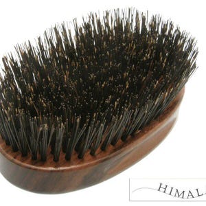 以下が含まれることがあります： 黒い毛のついた茶色の木製ヘアブラシ。ブラシは楕円形で、濃い木目模様があります。