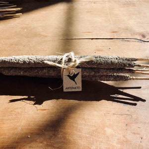 May include: A bundle of grey incense sticks tied together with twine and a brown paper tag that says "ARTEFAKTO" with a black hummingbird graphic.