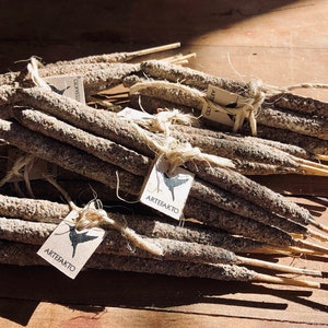 May include: A bundle of grey incense sticks with a brown wooden core, tied together with twine and labelled with a white tag that says "Artesanato".