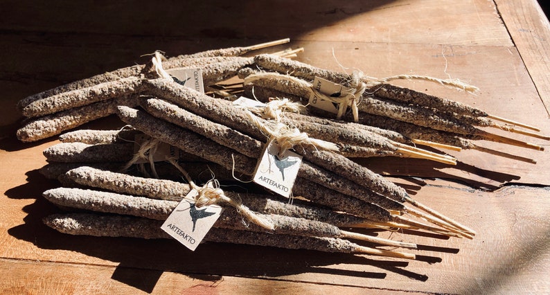 May include: A bundle of grey incense sticks with a brown wooden core, tied together with twine and labelled with a white tag that says "Artesanato".