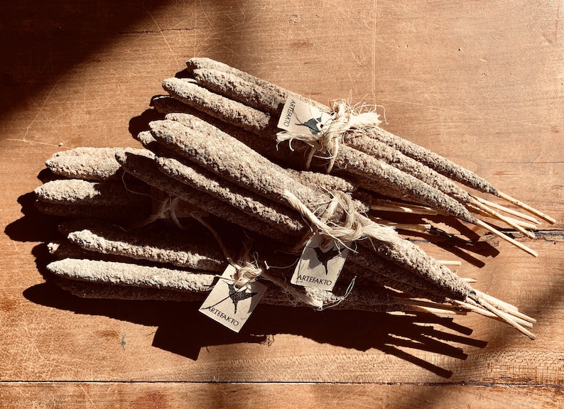 May include: A bundle of natural incense sticks tied together with twine. The sticks are made of a light brown material and have a rough texture. The sticks are labelled with the word "Artefakto" on a small tag.