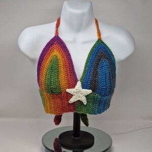 May include: A rainbow crochet halter top with a white crocheted star in the center. The top is made with a variety of colors, including purple, green, orange, and blue.