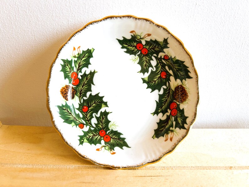 Round, Christmas-themed trinket dish made by Rosina China Co Ltd. The pattern is known as Queen's Yuletide and is a striking graphic of holly, berries and pine cones.