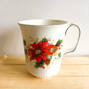 May include: A white ceramic mug with a black handle and the text "But First, Coffee" in a black, handwritten-style font. The mug is on a white surface.